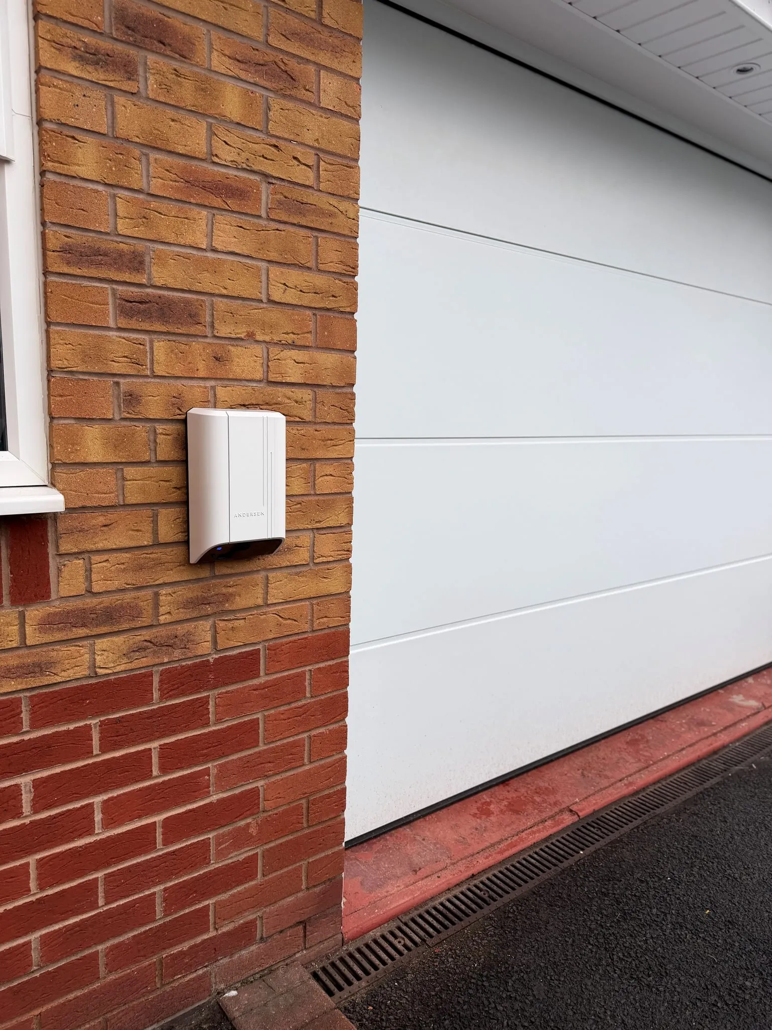 White Andersen Quartz EV charger on a brick wall beside a white garage door