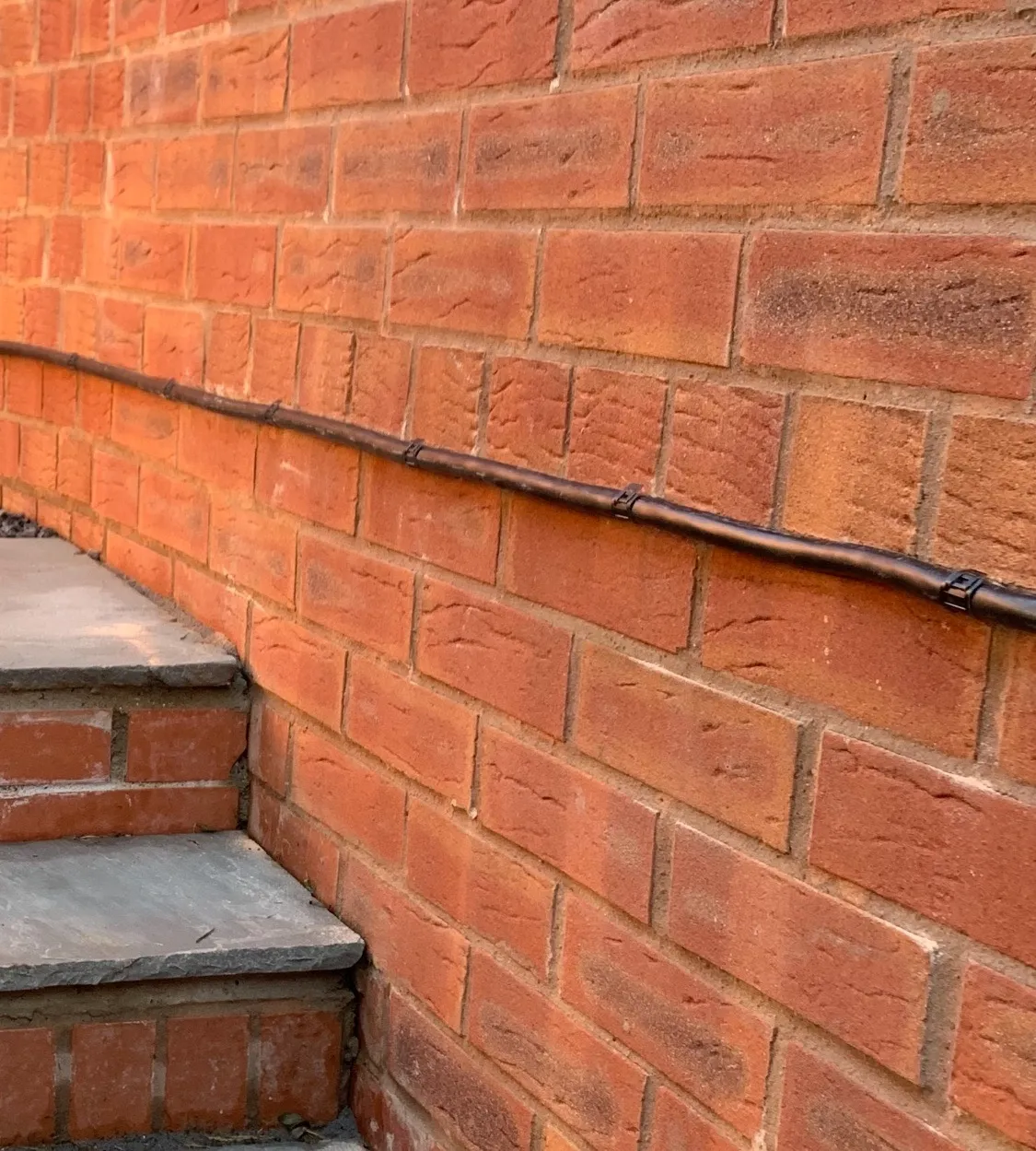 EV charger cable run along a red brick wall beside garden steps, held with D-Line clips