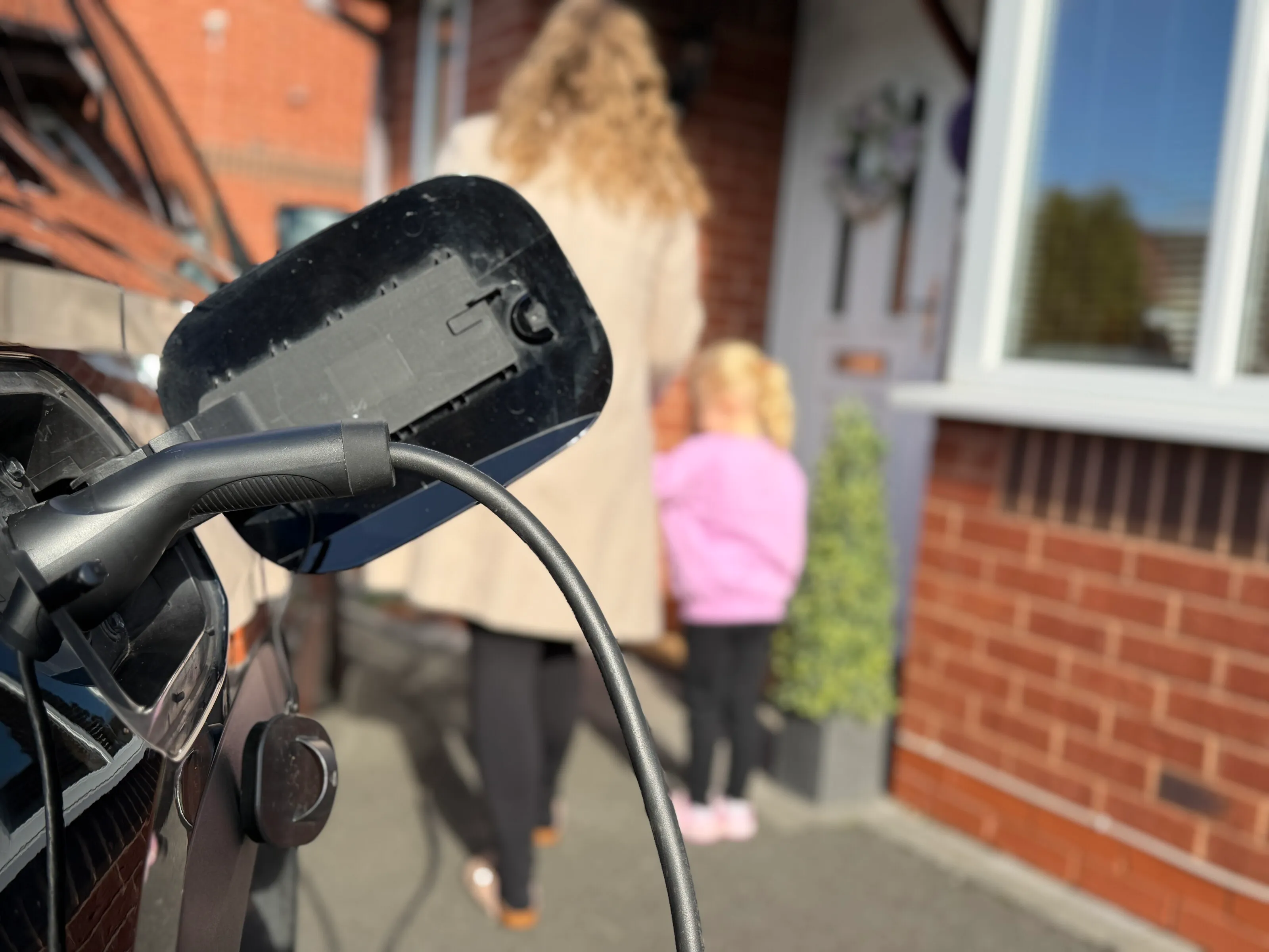 EV charging cable in the foreground with a family walking towards a house beyond
