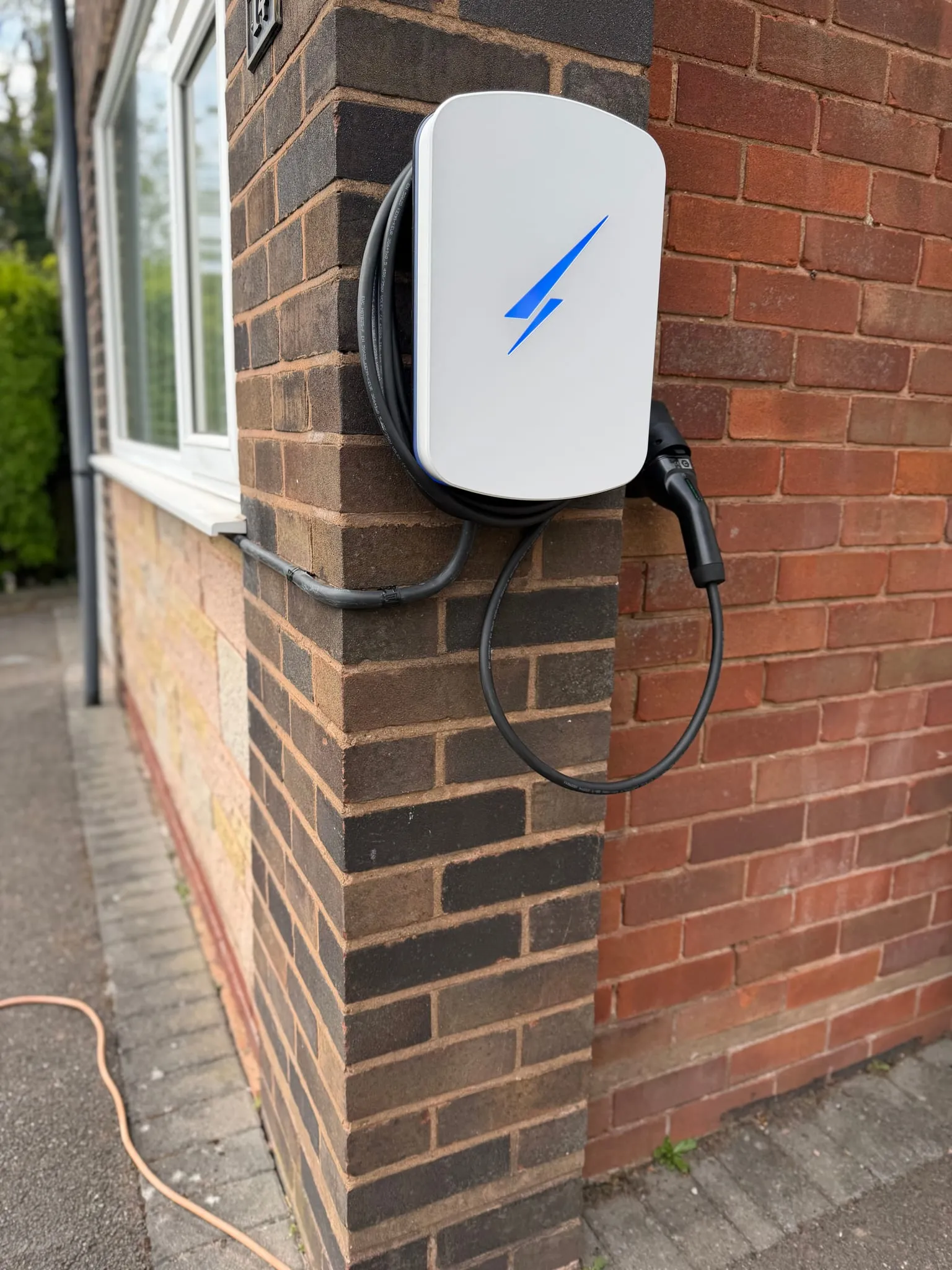 White Hypervolt EV charger with a blue illuminated logo on the corner of a two-tone brick pillar