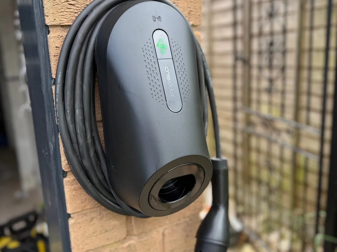 Black myenergi Zappi Glo EV charger with its cable coiled around it, on a brick pillar