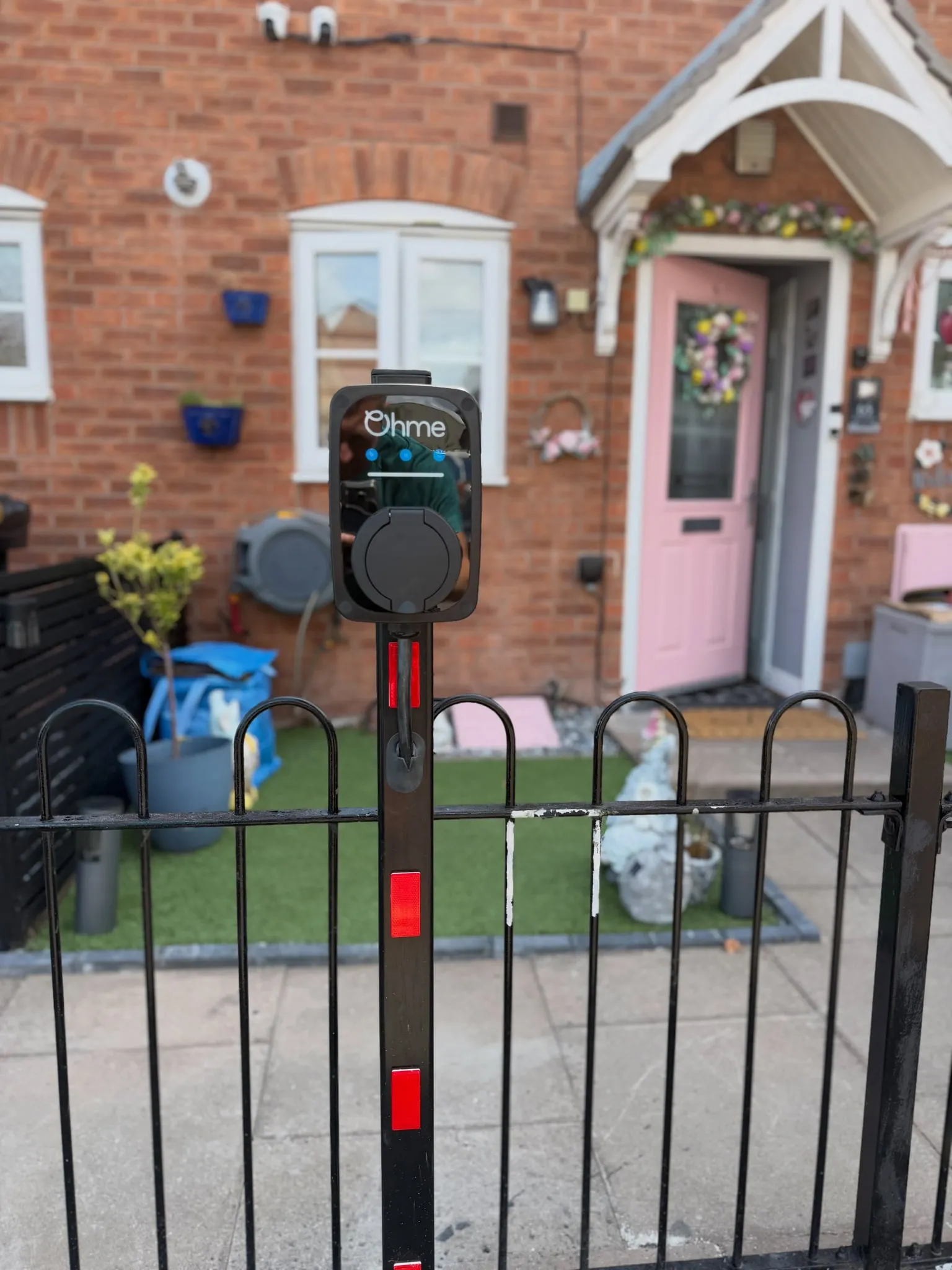 Post-mounted Ohme EV charger behind black railings at the front of a brick house