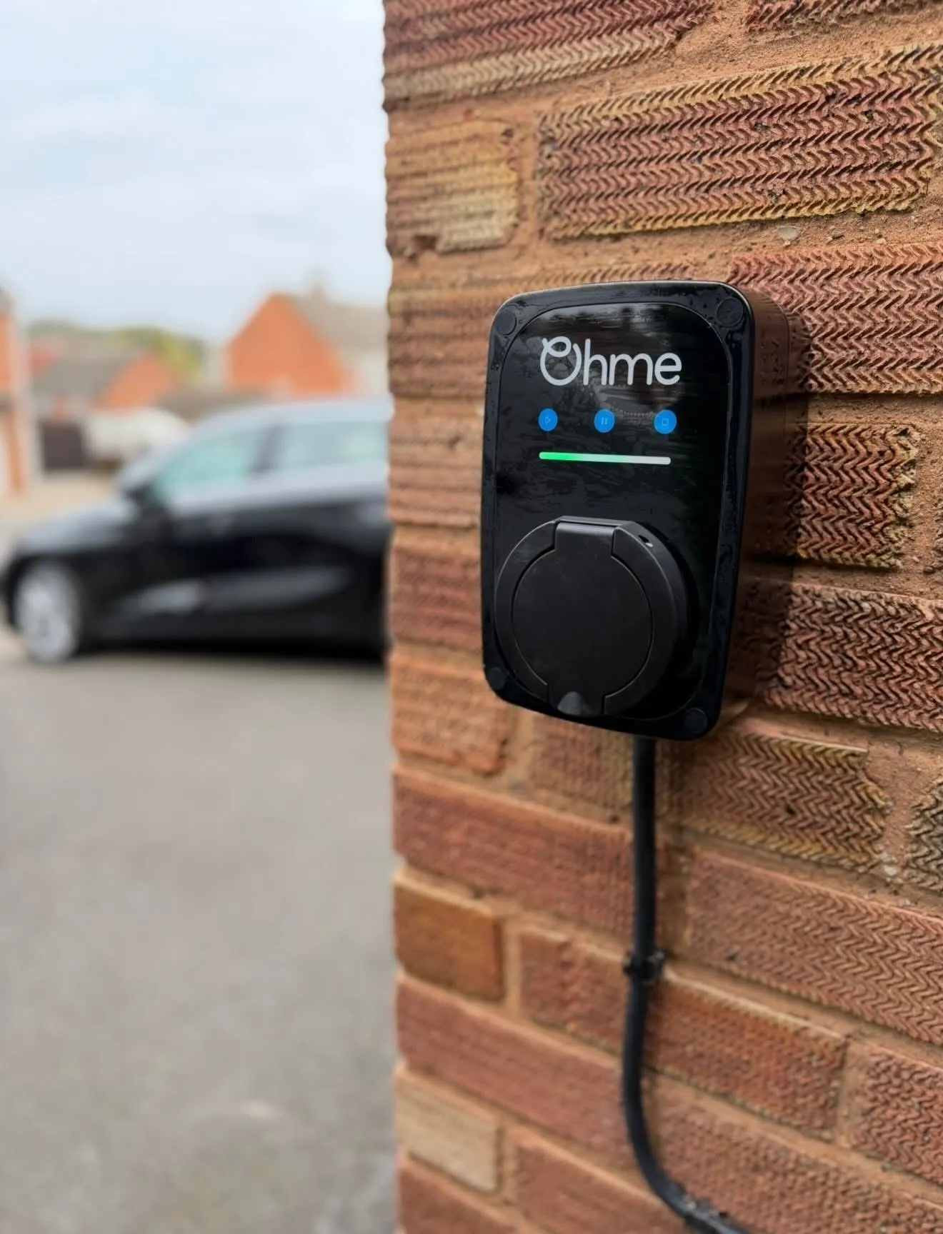 Close-up of an untethered Ohme EV charger with a covered socket, on a textured brick wall