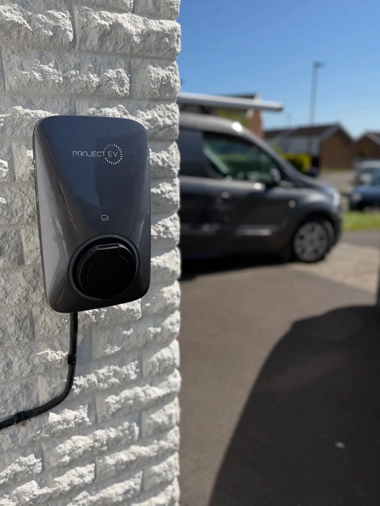Project EV charger mounted on a white painted brick wall beside a driveway