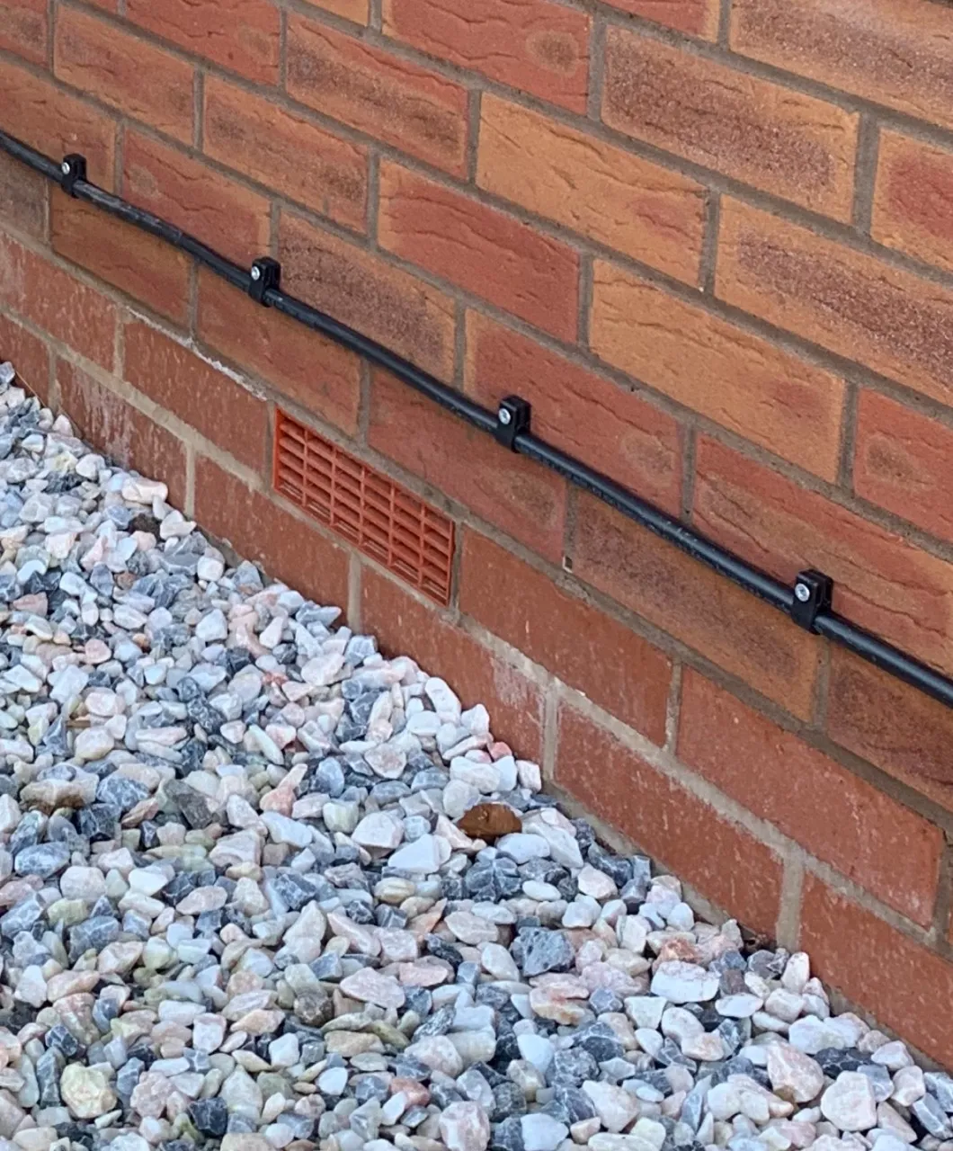 EV charger cable fixed along a red brick wall with regular cable cleats, above a gravel border
