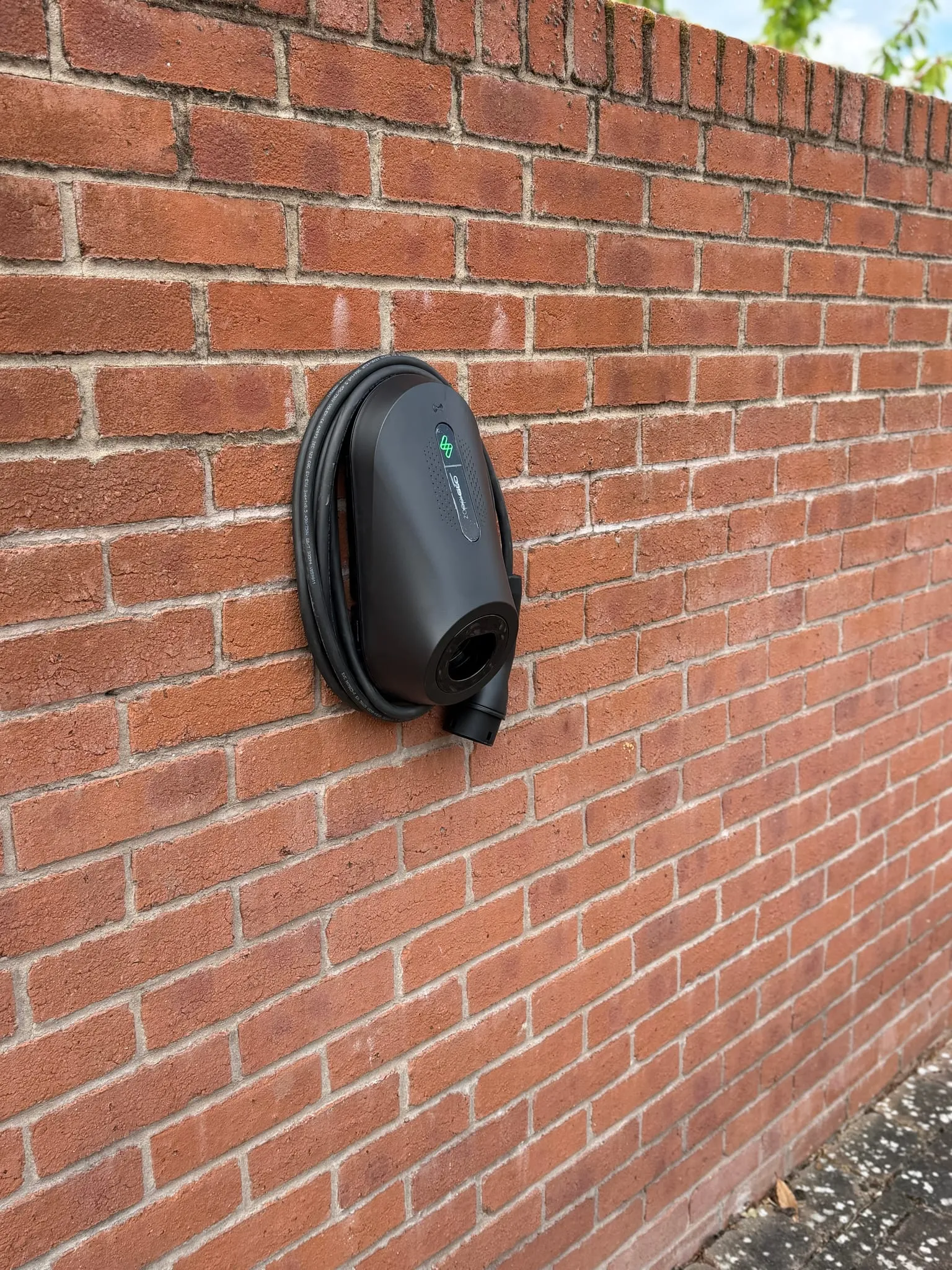 zappi GLO EV charger with its cable coiled around it, on a long red brick garden wall